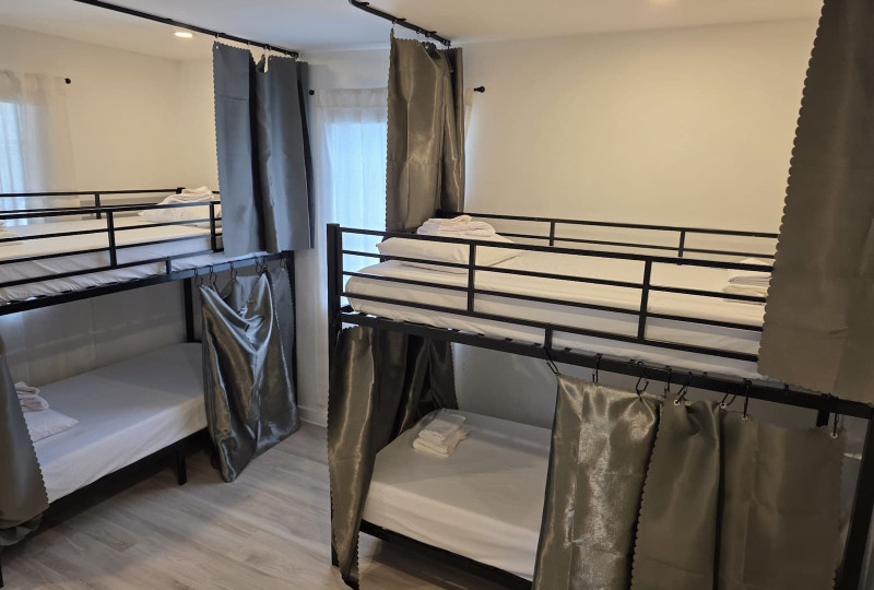 A clean and bright room with multiple black metal bunk beds, each with grey privacy curtains and fresh white linens.