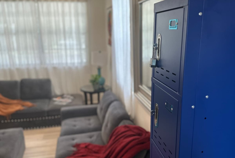 A bright blue industrial-style metal locker cabinet, partially seen from the side with multiple secure compartments and one visible padlock, in a residential setting.